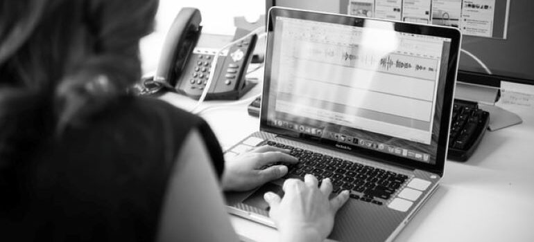 A black and white photo of a woman sitting at a desk and working on a laptop 