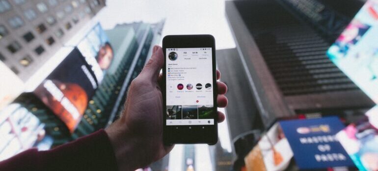 Person holding a phone with Instagram account opened on it pointed toward sky at Times Square
