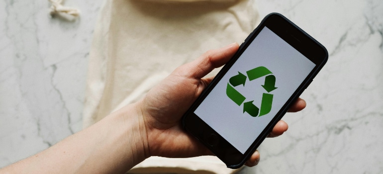 A hand holding a phone with a recycle logo, representing the tech innovations in the moving industry when it comes to eco-friendliness. 