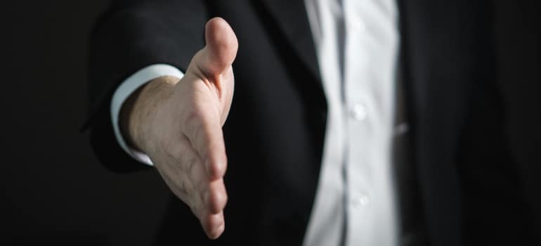 A person in a suit putting his hand forward to shake it. 