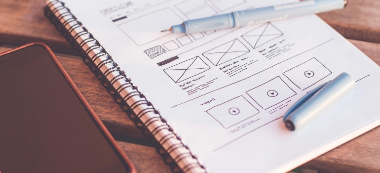 A close-up of a spiral notebook with wireframe sketches and a pen.