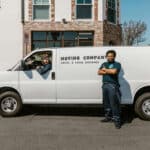 Two movers standing next to their moving company van.