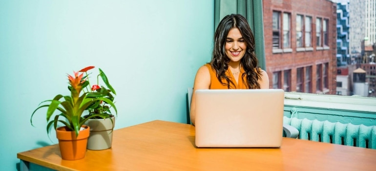 a woman sitting by the window looking at her laptop