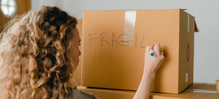 A person writing 'Fragile' on a box