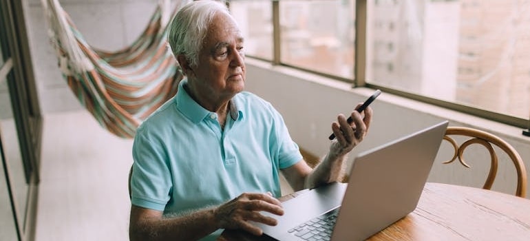 An elderly person using a laptop and a smartphone