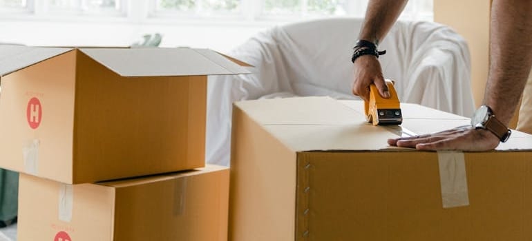 A person closing a carton box with duct tape