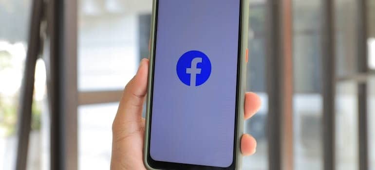 Person holding a phone showing the icon of Facebook, an app used by experts who know how to generate leads for a moving company