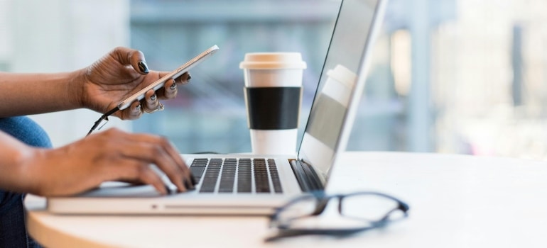 Person scrolling on phone and laptop looking for a moving company content in French language 