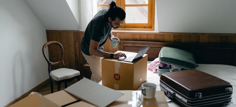 A person using a laptop while packing boxes