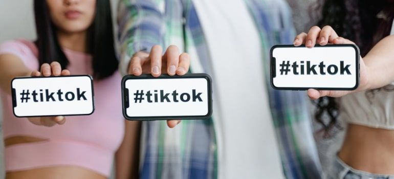 Young people holding phones with #tiktok, showing why movers should explore TikTok ads to reach a wider audience.