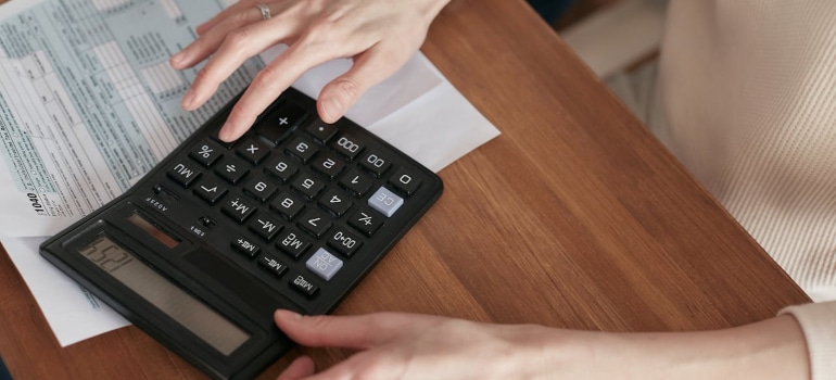 Hands using a calculator on a wooden desk beside a financial document.