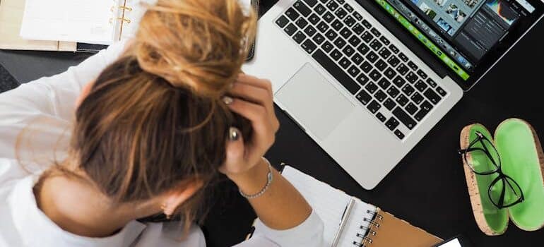 Woman sitting at a desk looking stressed with a laptop and notes, representing why moving companies struggle to tell what brings in jobs and feel uncertain about results.