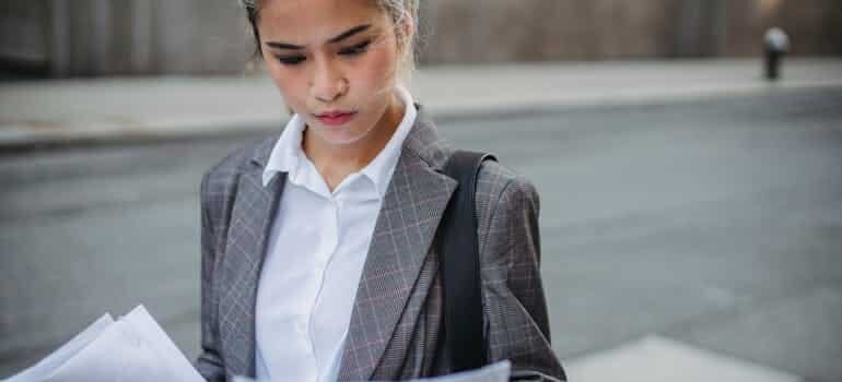 Person in a pinstriped suit holding documents on a city street, reviewing business paperwork in an urban setting.