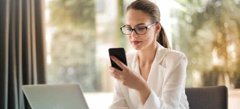 Professional woman using a smartphone and laptop at a desk, showing why moving companies struggle to tell what brings in jobs when leads come from multiple sources.