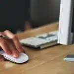 Hand using a computer mouse and holding a pen at a desk, illustrating why moving companies struggle to tell what brings in jobs when tracking is unclear.