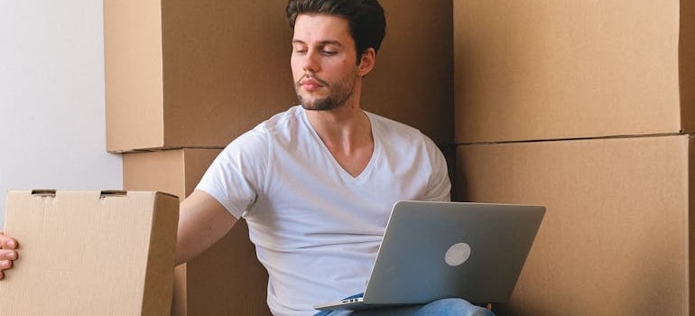 A person surrounded by boxes using a laptop to look for moving companies