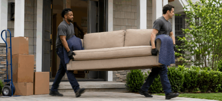 two movers carrying a couch out of a house.