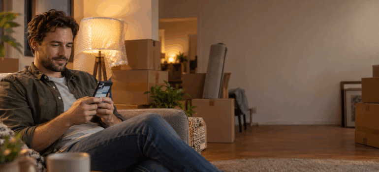a man texting a moving company through Google Business Profile chat on his couch surrounded by packed boxes